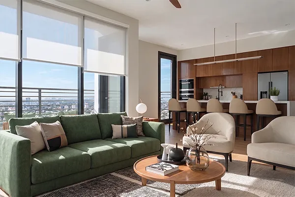 Living room in an Uptown Tucson residence with a green sofa, wood coffee table, and open kitchen, sunset view through floor-to-ceiling windows.