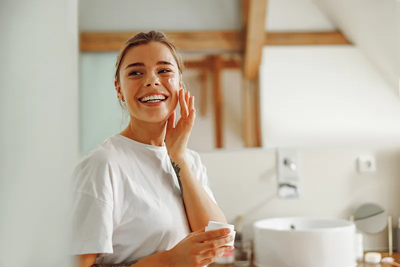 Woman smiling at a bathroom sink during her skincare routine