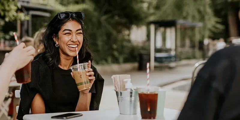 Woman laughing with an iced coffee at an outdoor café