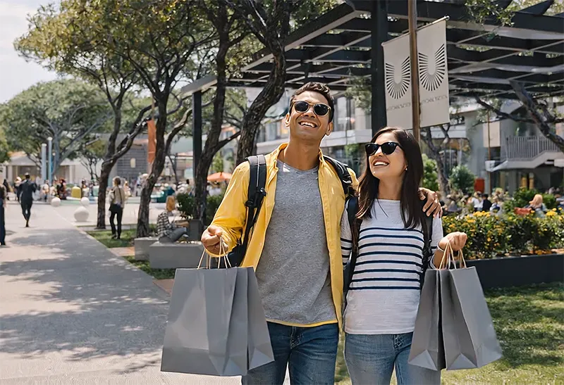 Couple carrying shopping bags along a shaded promenade