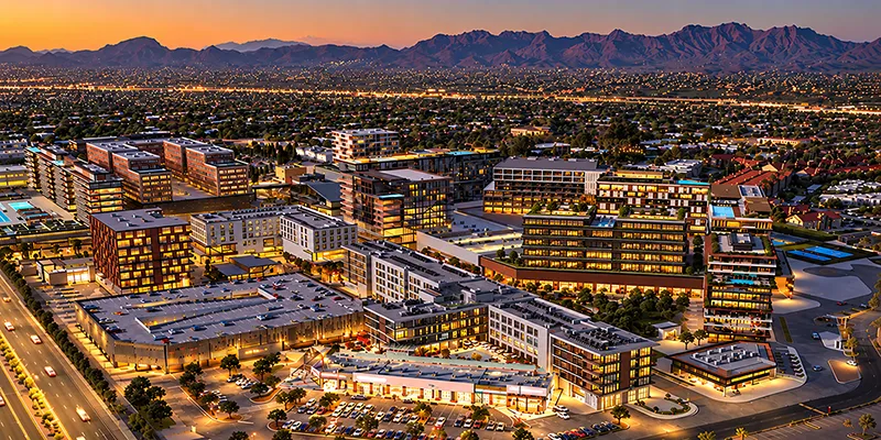 Aerial rendering of Uptown Tucson at dusk, with lit mid-rise residences, hotels and shops below desert mountains